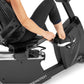 Person using black Freemotion r22.9 recumbent exercise bike with mesh backrest and foot pedals on white background