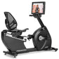 Black Freemotion r22.9 recumbent exercise bike with mesh backrest, foot pedals, and attached digital display screen showing w