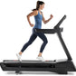 Woman running on black motorized treadmill wearing blue tank top and navy leggings, white sneakers