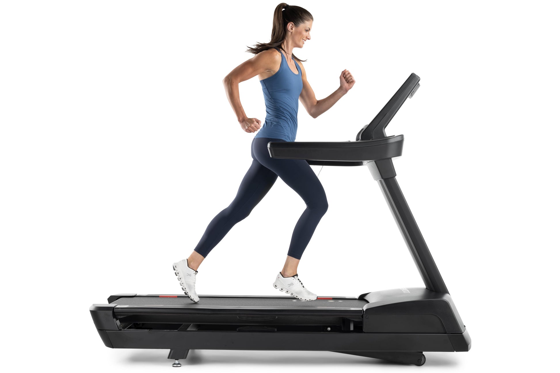 Woman running on black motorized treadmill wearing blue tank top and navy leggings, white sneakers