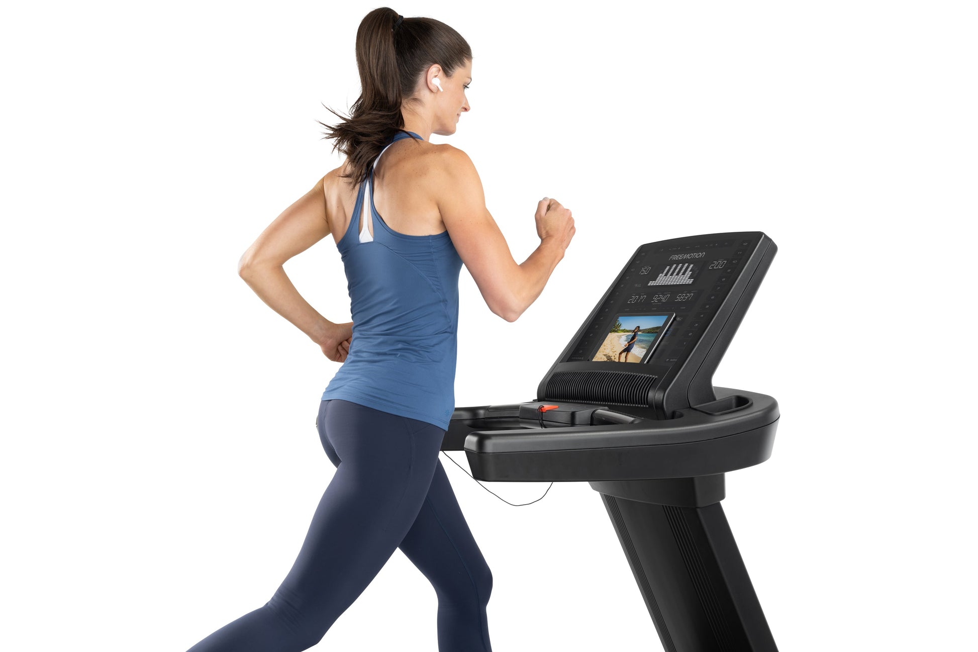 Woman running on black Freemotion treadmill with digital display, wearing blue tank top and navy leggings