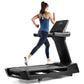 Woman running on black Freemotion treadmill wearing blue halter tank top and navy leggings, viewed from side on white backgro