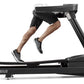 Man running on black t10.9b REFLEX treadmill with digital display, wearing black shorts and gray sneakers