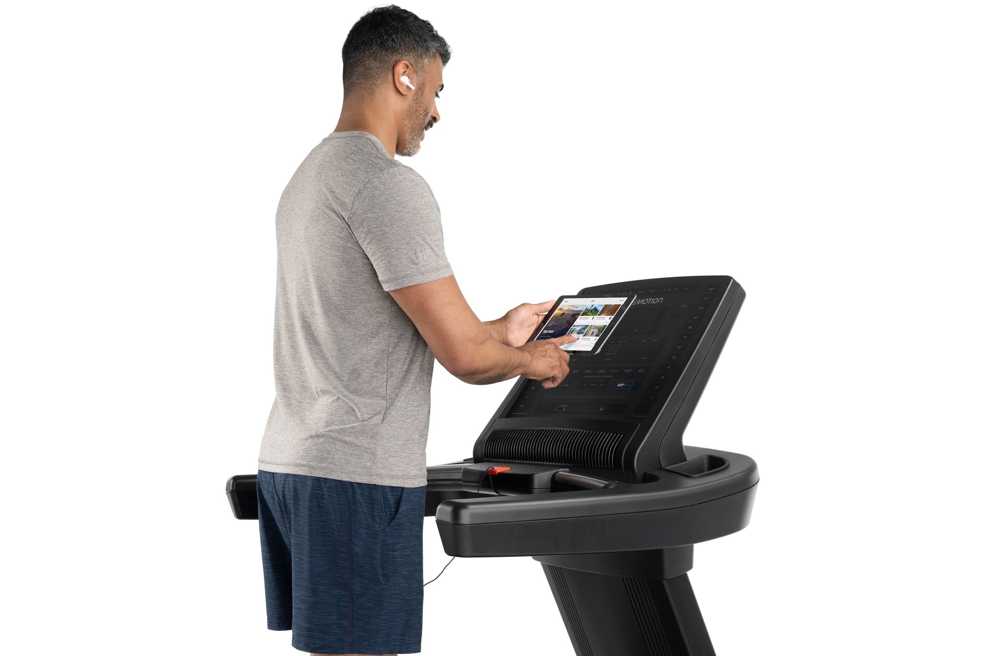 Man wearing gray t-shirt and navy shorts using black Freemotion treadmill with digital display on white background