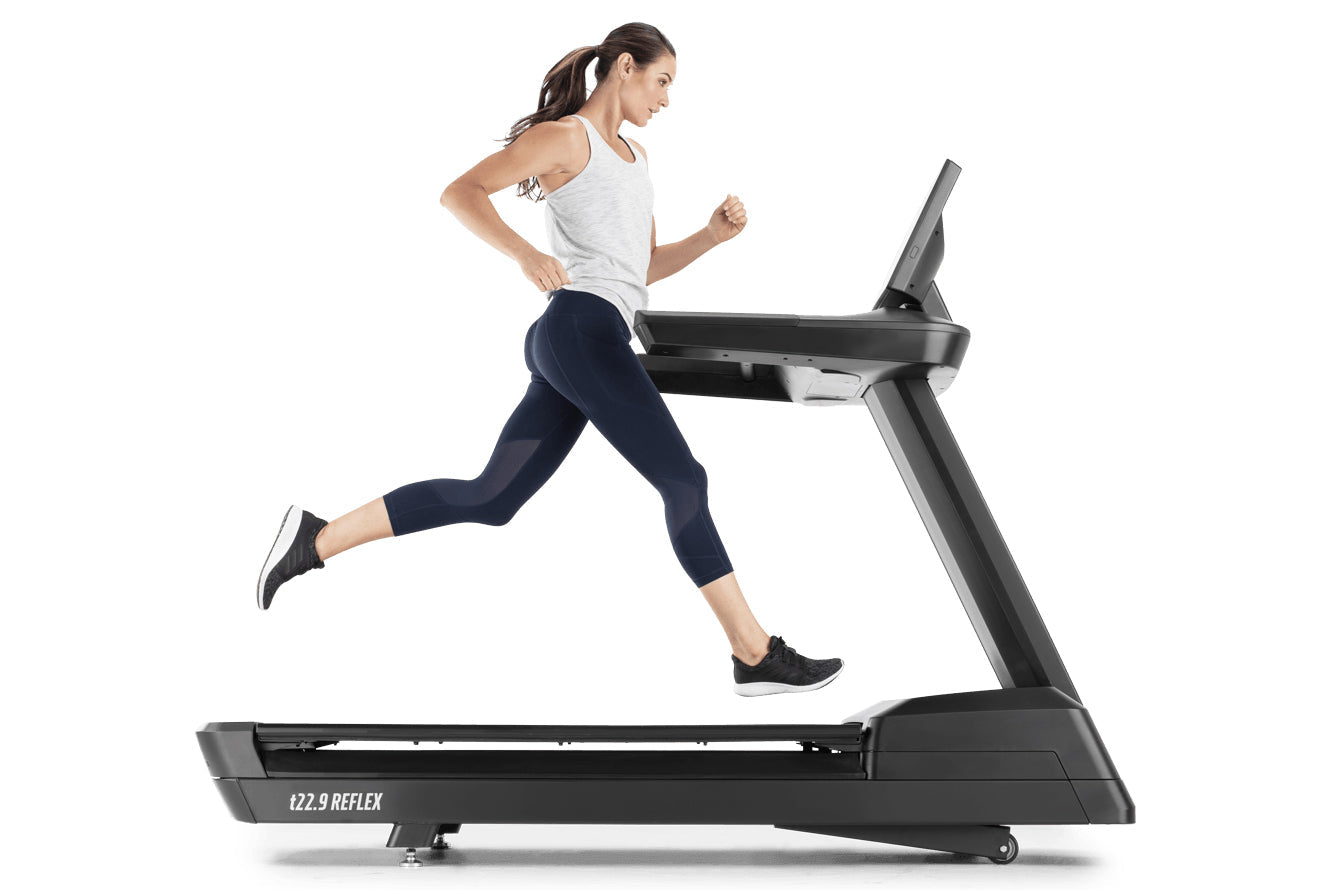 Woman running on black t22.9 REFLEX treadmill wearing gray tank top and navy capri leggings