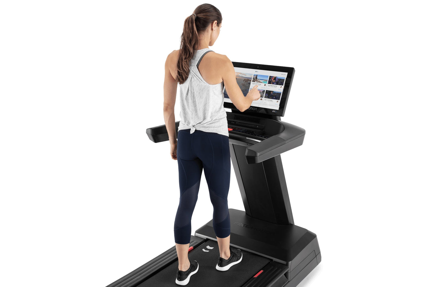 Woman wearing white tank top and navy capri leggings running on black Freemotion treadmill with interactive touchscreen displ