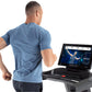 Man wearing blue heather t-shirt running on Freemotion treadmill with touchscreen display showing workout metrics