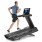 Man running on black Freemotion t22.9 REFLEX treadmill with touchscreen display, wearing blue t-shirt and black shorts