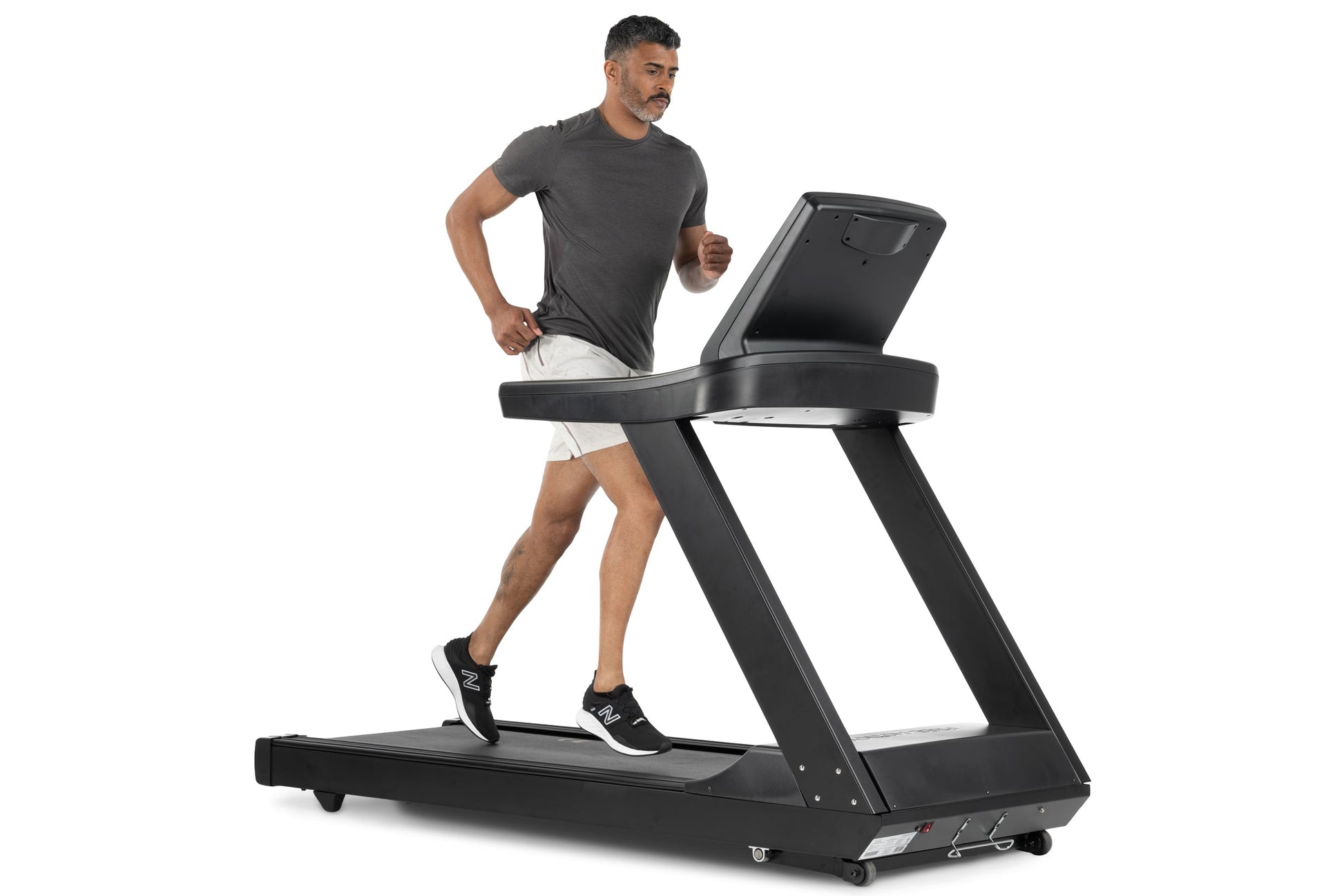 Man running on black Freemotion t8.9b treadmill with digital display, wearing charcoal t-shirt and white shorts