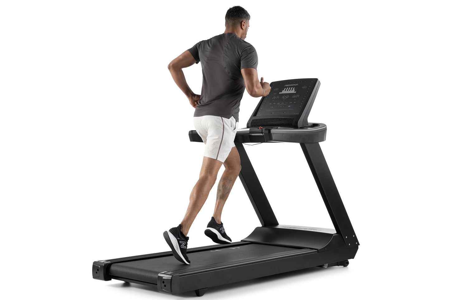 Man running on black Freemotion t8.9b treadmill with digital display, wearing gray t-shirt and white shorts