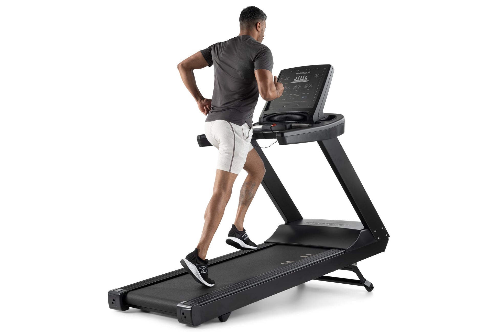 Man running on black Freemotion t8.9b treadmill with digital display console, wearing dark t-shirt and white shorts