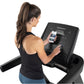 Woman wearing black racerback tank top using Freemotion t8.9b treadmill while holding smartphone displaying workout app on wh