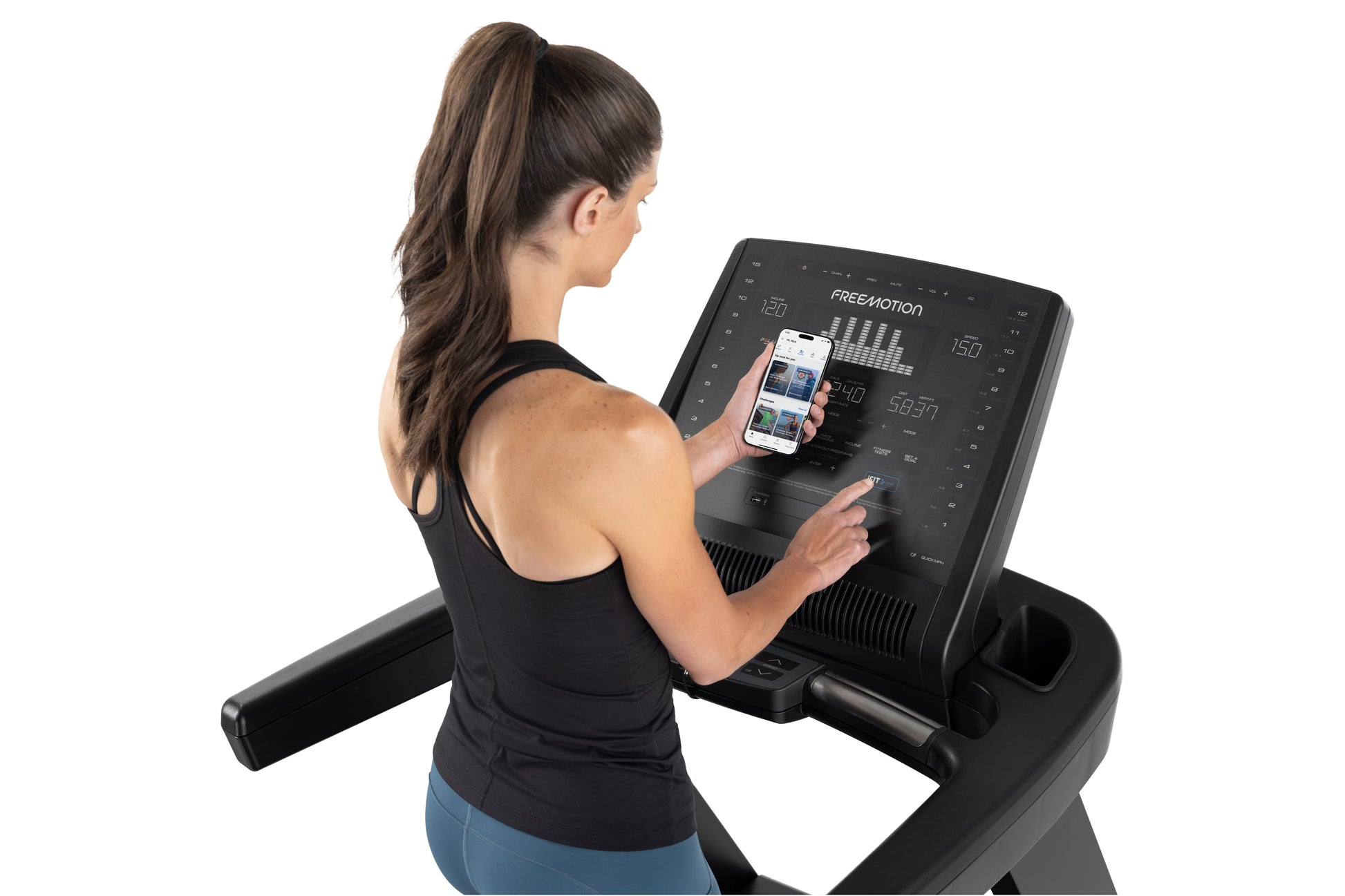 Woman wearing black racerback tank top using Freemotion t8.9b treadmill while holding smartphone displaying workout app on wh