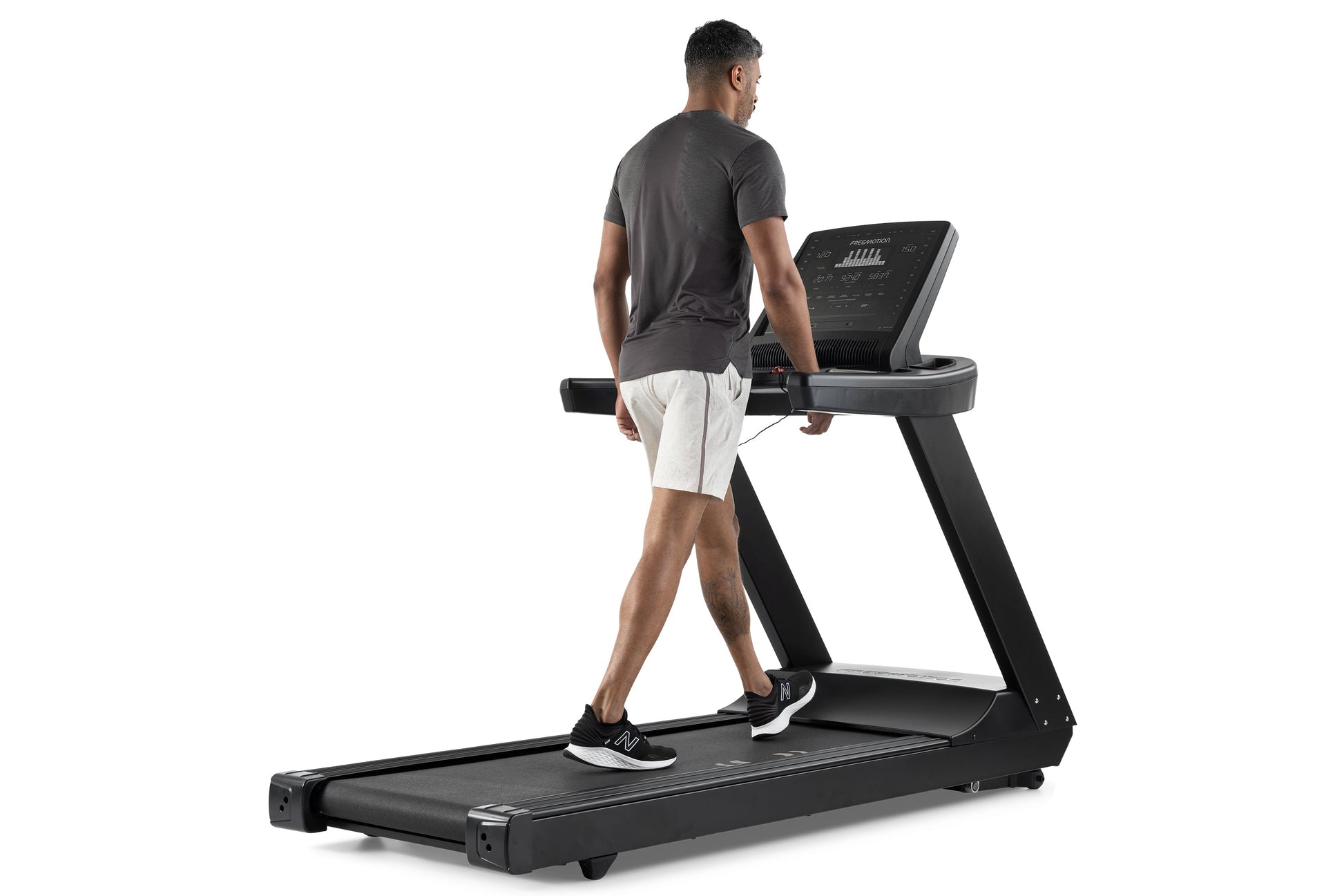 Man jogging on black Freemotion t8.9b treadmill with digital display, wearing gray shirt and white shorts