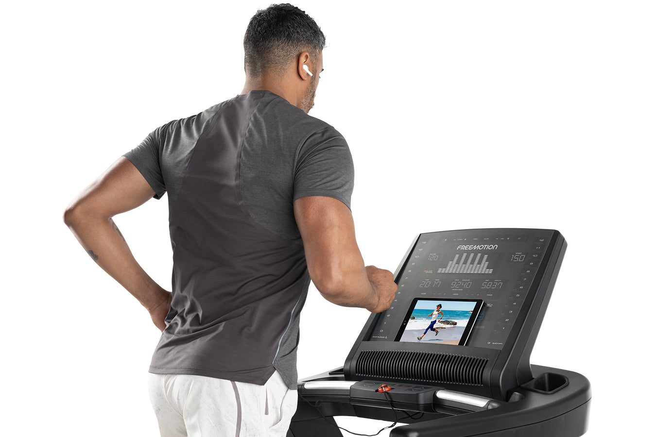 Man wearing charcoal t-shirt and white shorts using Freemotion t8.9b treadmill with digital display showing workout metrics