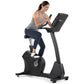 Woman in gray tank top and navy leggings using black Freemotion upright exercise bike with digital display, against white bac