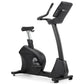 Black upright exercise bike with digital display console, padded seat, curved handlebar, and stabilizing base on white backgr