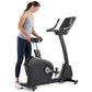 Woman wearing gray tank top and navy leggings using black Freemotion upright exercise bike with digital display on white back