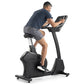 Man using black Freemotion upright exercise bike with digital display, wearing navy t-shirt and gray shorts on white backgrou
