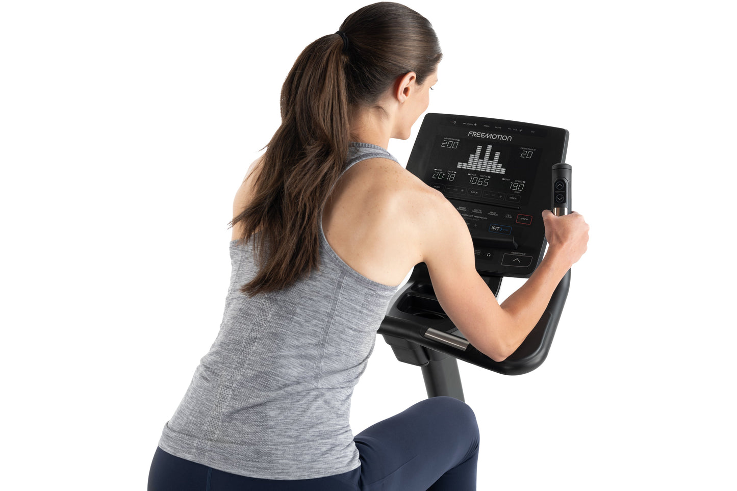 Woman wearing gray sleeveless top and navy pants using Freemotion u10.9b upright exercise bike with black digital display con