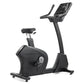 Black upright exercise bike with digital display console, padded seat, and stationary handlebars on white background