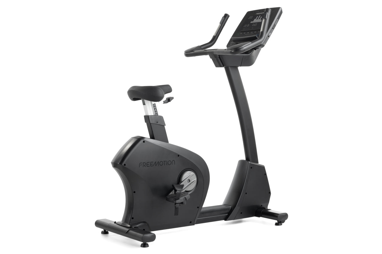 Black upright exercise bike with digital display console, padded seat, and stationary handlebars on white background