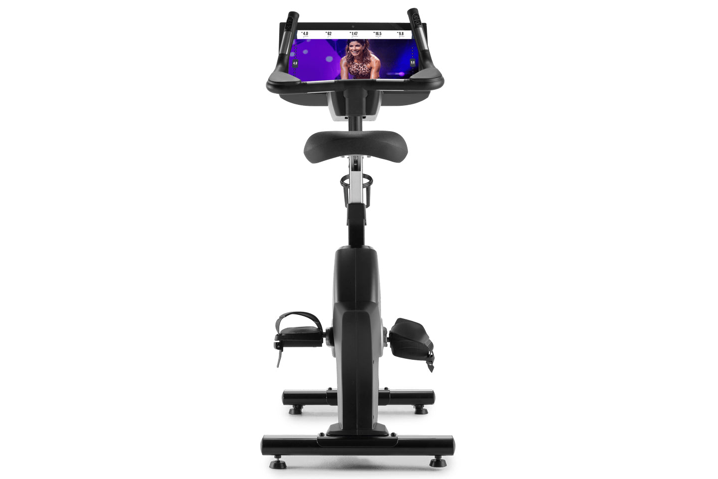 Black upright exercise bike with tablet holder displaying fitness class, padded seat, dual handlebars, and foot pedals on whi