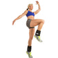 Woman wearing blue sports bra and gray shorts demonstrating adjustable black ankle weights with neon yellow accents while jum