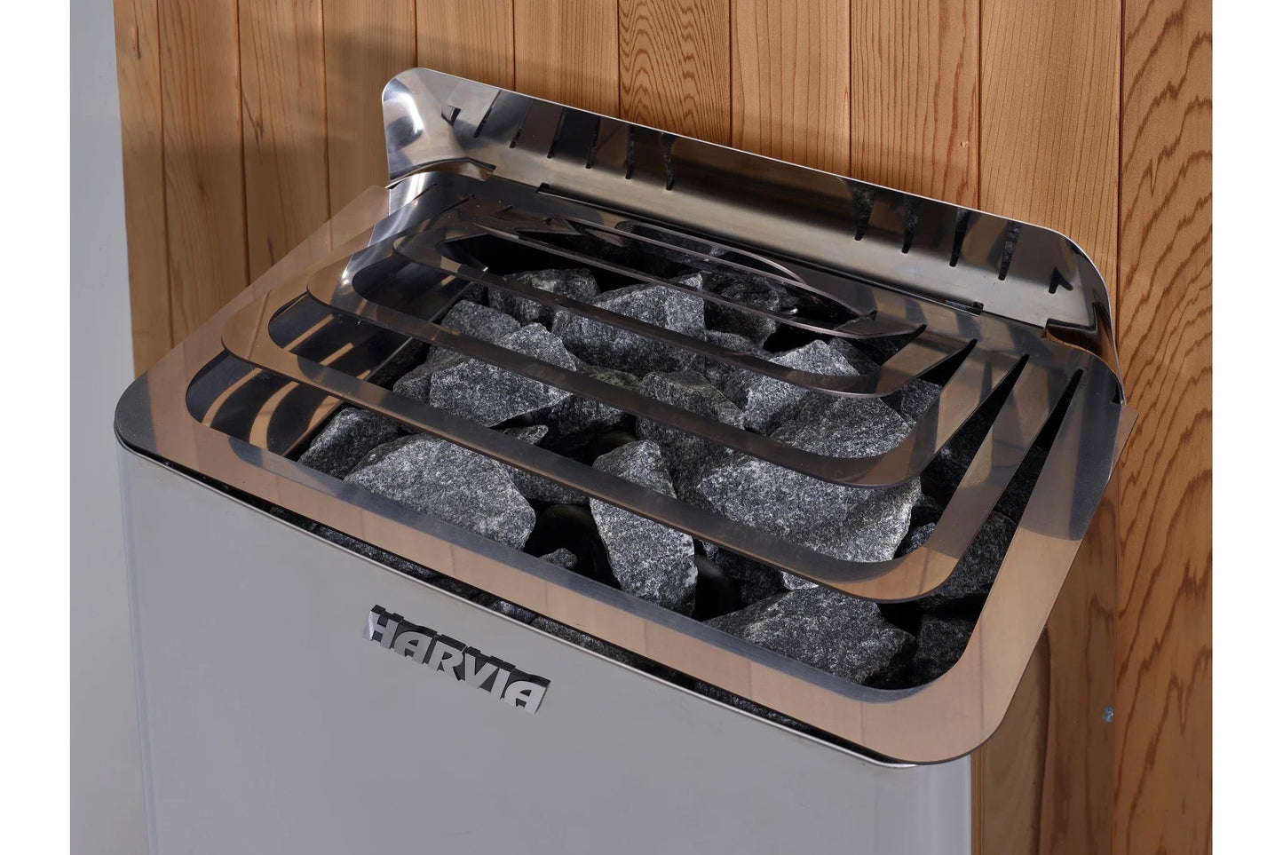 Harvia Arlberg sauna heater with gray stones visible in open compartment, mounted on wooden wall background
