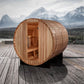 Golden Designs Arosa barrel sauna in light wood with open door showing interior benches, positioned on wooden deck with snow-
