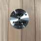 Brushed metal circular plate labeled MP3 AUX INPUT MAX 175mV mounted on light wood paneling, flat lay