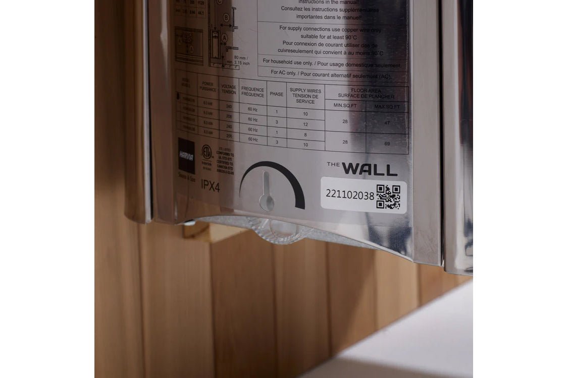 Close-up of sauna heater control panel showing technical specifications, wiring diagram, and QR code on white label mounted o