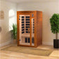Wood infrared sauna cabin with glass front door and black heating panels inside, displayed in home setting with potted plants