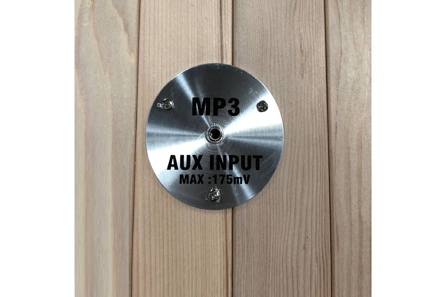 Brushed metal circular control panel labeled MP3 AUX INPUT MAX 175mV mounted on light wood sauna wall