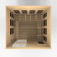 Natural wood infrared sauna cabin with wooden benches, black heater panels, and overhead infrared heating elements, viewed fr