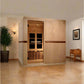 Light wood infrared sauna cabin with glass door and dark trim, installed in modern home interior with potted plant and wooden