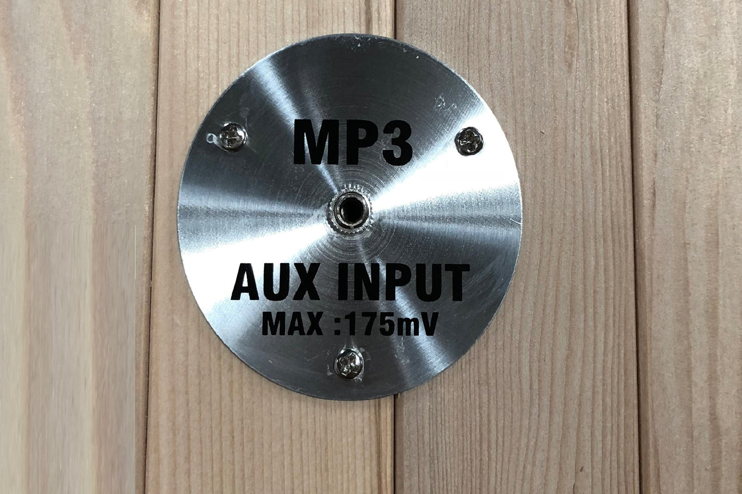 Polished stainless steel MP3 auxiliary input panel with center jack and mounting screws on wooden background