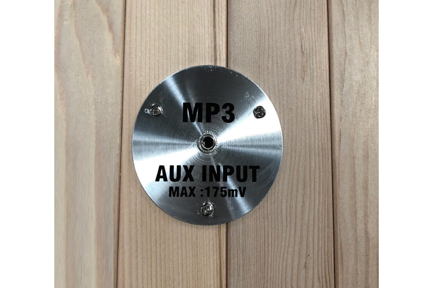 Brushed metal circular panel with MP3 and AUX INPUT MAX 175mV text, mounted on light wood background
