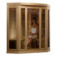 Natural wood corner sauna with glass and slatted cedar panels, woman sitting inside wearing white towel on wooden bench