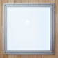 Silver-framed white square mirror with metal corners mounted on light wood wall