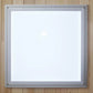 Silver-framed square mirror with white center and corner mounting hardware on wooden background