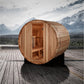 Cedar wood barrel sauna with open door showing interior benches, positioned on wooden deck with snow-capped mountains in back