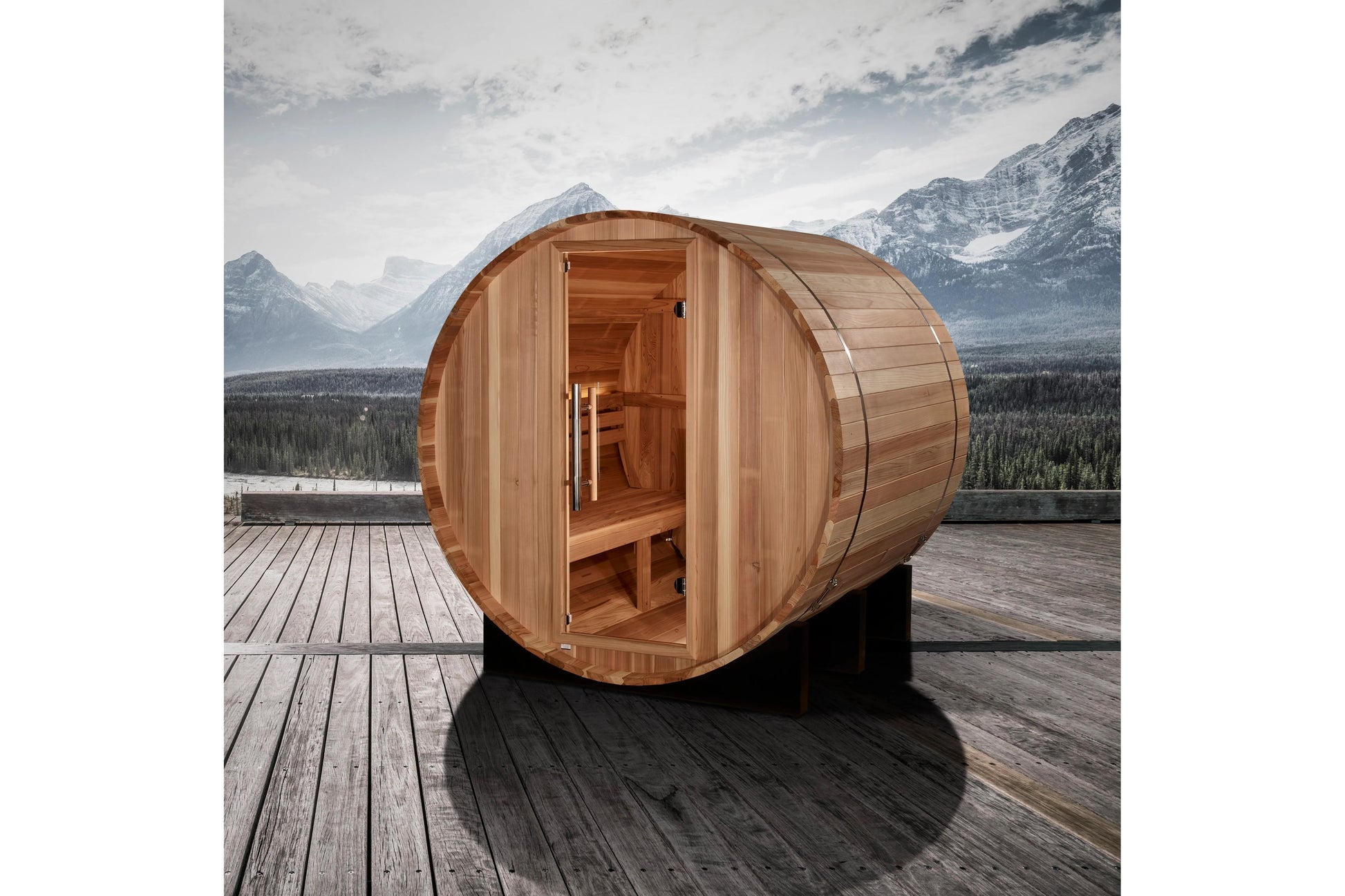 Cedar wood barrel sauna with open door showing interior benches, positioned on wooden deck with snow-capped mountains in back