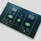 Dark teal sauna control panel with digital temperature and timer displays, green illuminated buttons for power, heat, and lig
