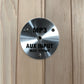 Brushed silver circular control panel labeled MP3 AUX INPUT MAX 175mV mounted on light wood sauna wall