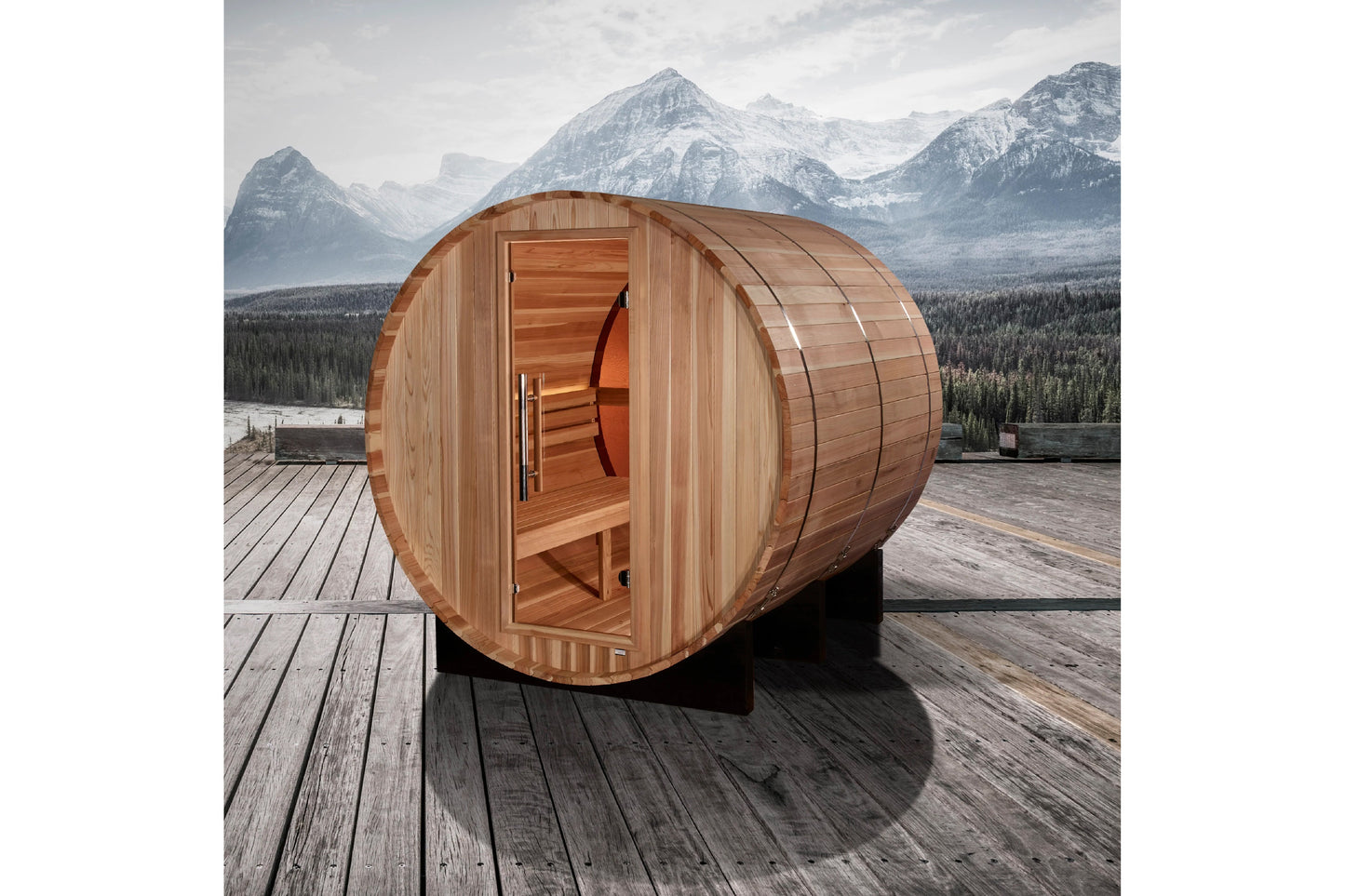 Cylindrical cedar barrel sauna with open door showing wooden interior benches, positioned on wooden deck with snow-capped mou