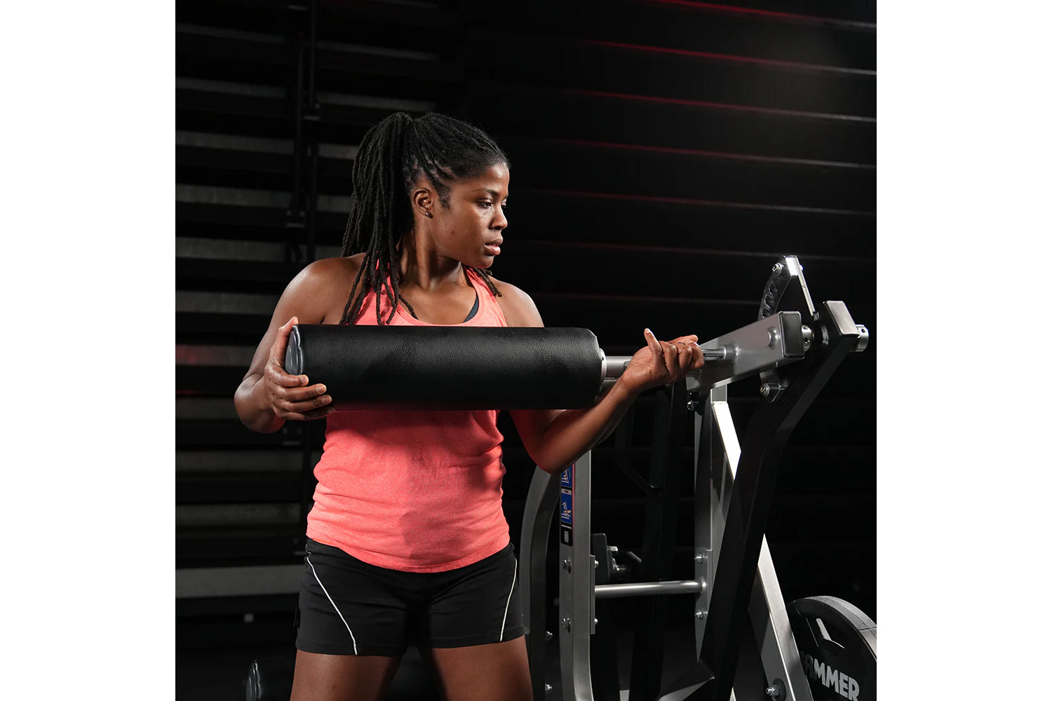 Woman wearing coral halter tank top and black shorts using Hammer Strength assisted leg press machine in gym setting