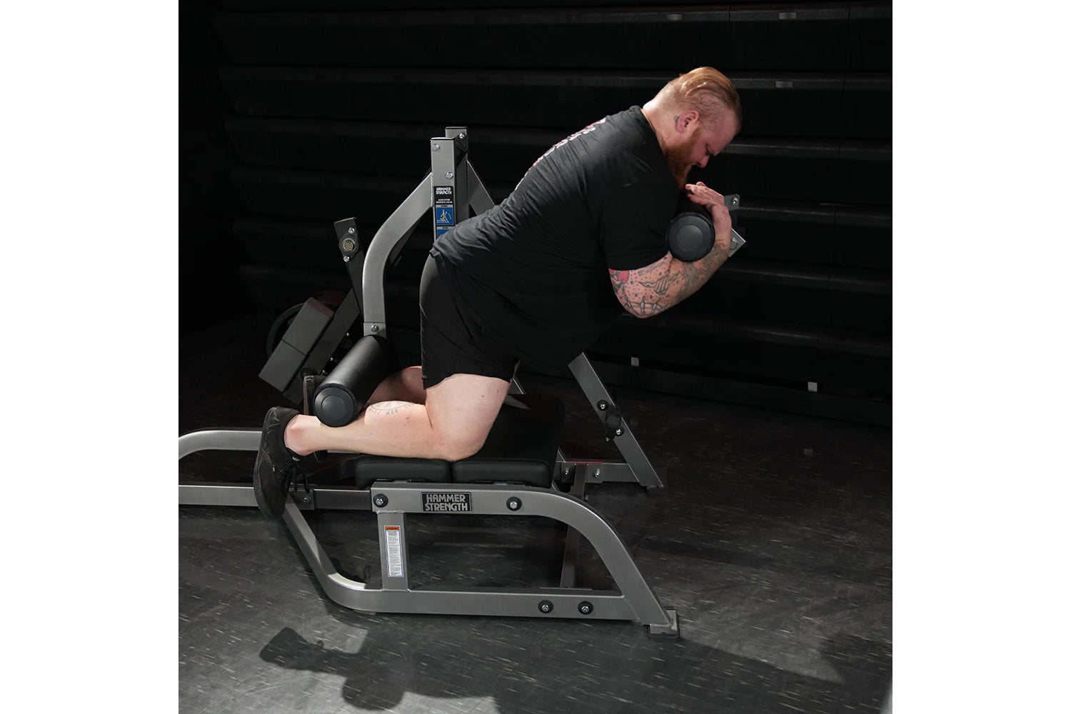 Man using Hammer Strength leg curl machine with adjustable weights, demonstrating exercise form in gym setting