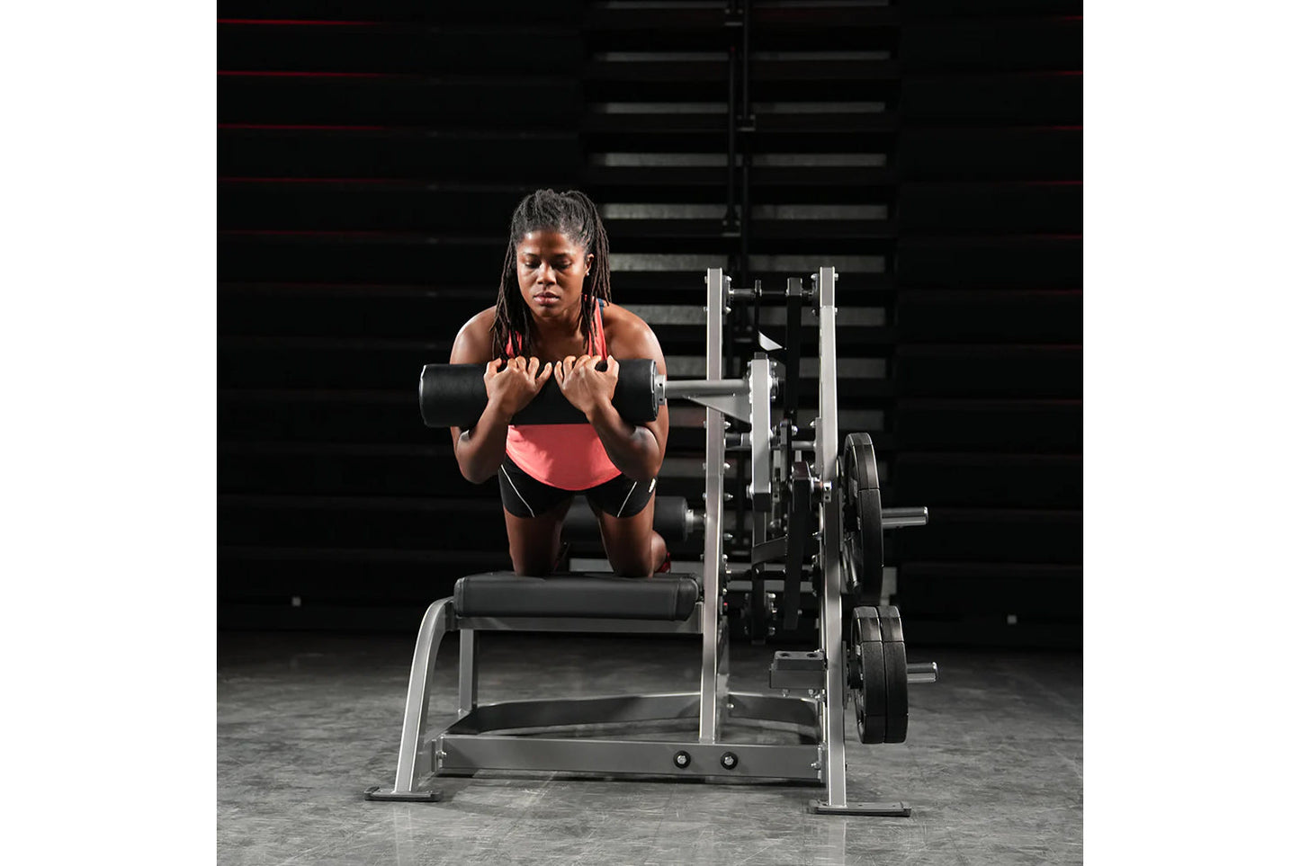 Woman wearing coral sports bra and black shorts performing dumbbell exercise on weight bench in gym setting