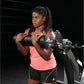 Woman wearing neon pink sleeveless tank top and black shorts performing dumbbell exercise on weight machine